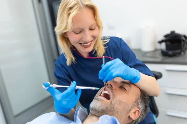 鎮痛剤麻酔注射だ 現代の歯科事務所で患者の歯を調べる歯科医 コピースペースで切り取られた画像を閉じます 青い制服の女医 — ストック写真