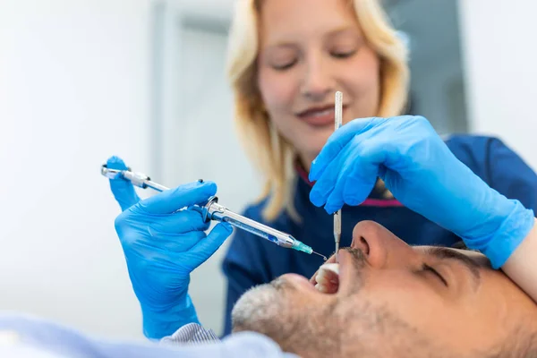 stock image Painkiller anesthesia injection. Dentist examining a patient's teeth in modern dentistry office. Closeup cropped picture with copyspace. Female Doctor in blue uniform.