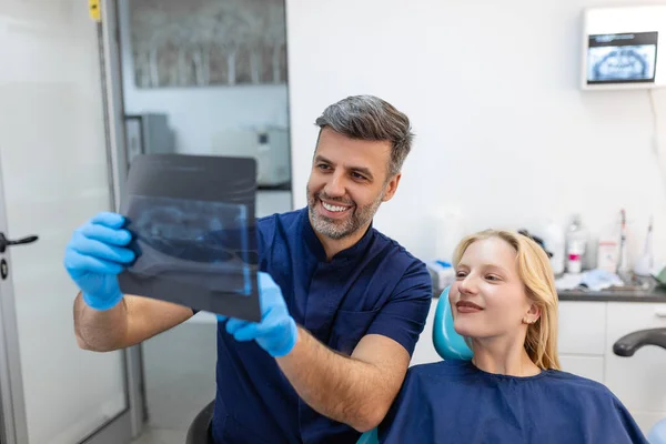 Doctor talking with her patient and teaching a radiograph. Dentist concept of woman sitting in a dental chair while her dentist reads out an x-ray scan