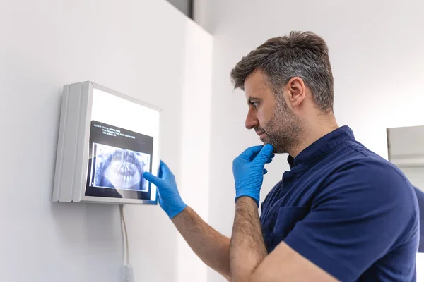 health dental professional in blue scrubs examining dental x-ray on computer screen. Dentists looking to x-ray scan on monitor at dental clinic.