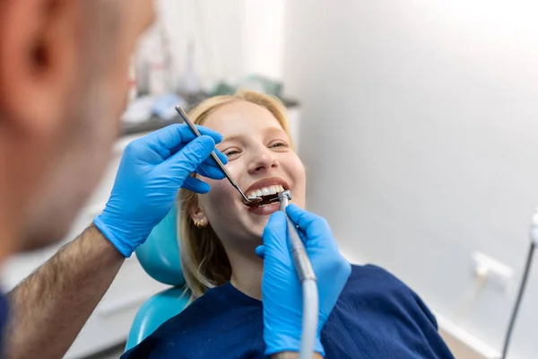 Smiling dentist communicating with young woman while checking her teeth during dental procedure at dentist\'s office.