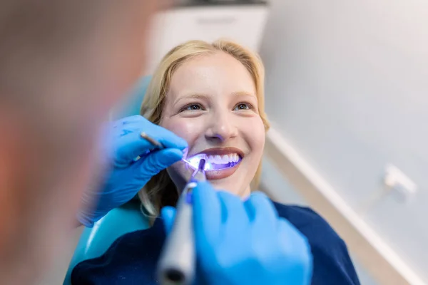 Patient in the dental clinic. Teeth whitening UV lamp with photopolymer composition. Young woman during teeth whitening procedure with curing UV light at dentist\'s office.
