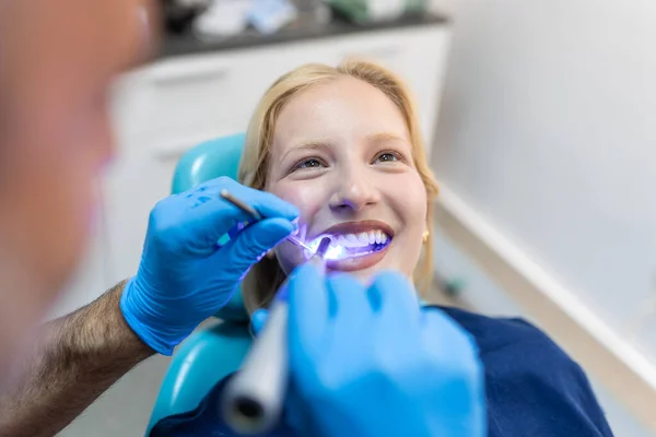 Patient in the dental clinic. Teeth whitening UV lamp with photopolymer composition. Young woman during teeth whitening procedure with curing UV light at dentist\'s office.