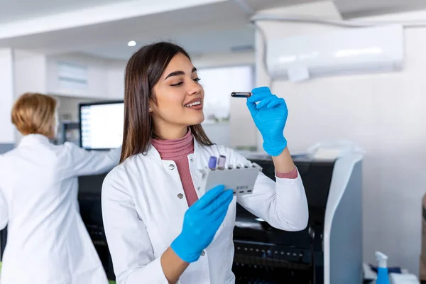 stock image Laboratory assistant putting test tubes into the holder. Scientist doctor looking at blood test tube working at biochemistry experiment in microbiology hospital laboratory.