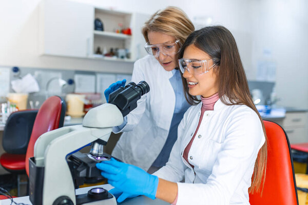 Medical Science Laboratory: Beautiful Scientist Looking Under Microscope Does Analysis of Test Sample. Young Specialists, Using Advanced Technology Equipment