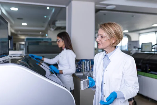 女性研究者血液サンプルを分析器医療機器に試験管を入れる 科学者は製薬研究所で現代医療機器と仕事をする — ストック写真