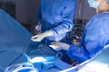 Cerrahlar, hastane ameliyathanesinde ameliyat öncesi hazırlık yaparken monitörlere bakar. Erkek cerrah, cerrahi laparoskopi aletleriyle çalışan hastalara bakar..