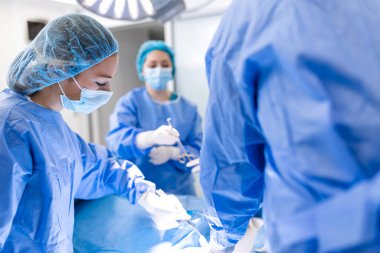 Doktor ve hemşire tıbbi ekibi hastanedeki acil serviste ameliyat yapıyor. Asistan ameliyat sırasında cerrahlara makas ve aletler dağıtıyor.