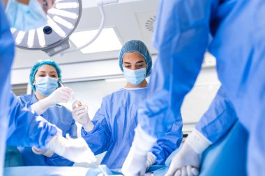 Medical team performing operation. Group of surgeon at work in operating theatre toned in blue. Doctor operation in operation room at hospital concept for insurance advertising.
