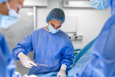 Tıbbi ekip operasyon yapıyor. Ameliyathanede çalışan bir grup cerrah mavi tonda. Sigorta reklamları için hastane konseptinde doktor operasyonu.