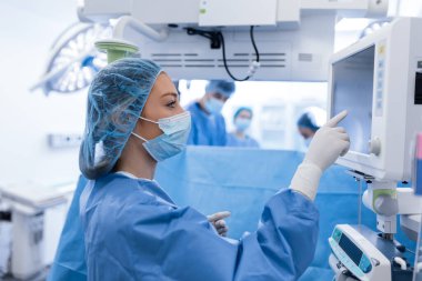 Ameliyat öncesi anestezi makinesi hazırlayan önlüklü ve koruyucu maskeli genç bir kadın doktor portresi.