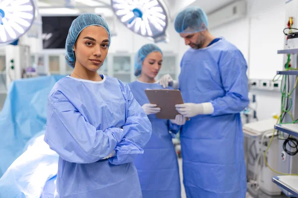 stock image Portrait of female woman nurse surgeon OR staff member dressed in surgical scrubs gown mask and hair net in hospital operating room theater making eye contact smiling pleased happy looking at camera