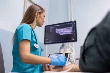 Kadın doktor, ofisinde hastanın kol damarlarını ultrason muayenesi yapıyor. Genç adam klinikte ultrason taramasını geçiyor. Doktor işi. Tıbbi araştırma.