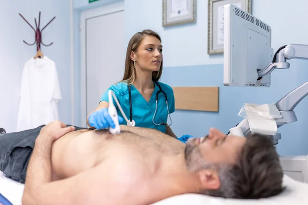 Female medic using modern ultrasound equipment and examining heart of male patient lying on medical table during diagnostic in hospital