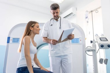 MRI taramasından önce erkek doktor kadına bilgi veriyor. Özel tıp kliniğinde manyetik rezonans görüntüleme teknolojisi.