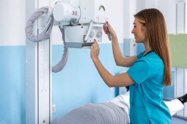 Hastanede, Yatakta Yatan Adam 'ın Düşük Açı Fotoğrafı' nda, Kadın Teknisyen X-Ray Makinesini düzeltti. Kırıklar, kırık uzuvlar, yaralar, kanser ya da tümör taraması. Modern Hastane