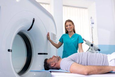 Bayan doktor, hastanın tomografisine bakıyor. Üniformalı doktor hastanede yatan bir hastayla tomografi makinesi kullanıyor.