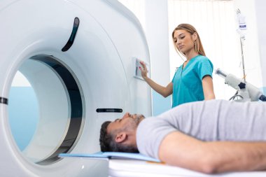 Bayan doktor, hastanın tomografisine bakıyor. Üniformalı doktor hastanede yatan bir hastayla tomografi makinesi kullanıyor.