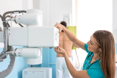 Hastane Radyoloji Odası: Erkek, X-Ray makinesinin yanında dikilirken, kadın doktor bunu düzeltiyor. Sağlıklı Hasta, Doktor 'un yardımıyla sağlık muayenesinden geçiyor..