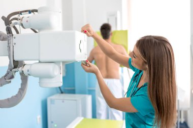 Hastane Radyoloji Odası: Erkek, X-Ray makinesinin yanında dikilirken, kadın doktor bunu düzeltiyor. Sağlıklı Hasta, Doktor 'un yardımıyla sağlık muayenesinden geçiyor..