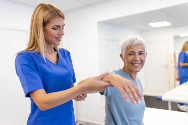 Doktor ortopedik son sınıf kadınına kemik erimesi tedavisi uygulamasını modern klinikte öğretiyor. Fizyoterapist, kas rehabilitasyonu sırasında kadın hastaya yardım ediyor.