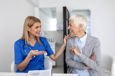 Beyaz üniformalı genç kadın doktor ya da pratisyen hekim özel hastanedeki yaşlı kadın hastaya danışıyor. Kadın terapist klinikte danışmanlık yapan kadın müşteriyle konuşuyor..