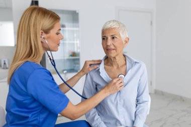 Genç bayan doktor klinikte steteskoplu yaşlı bir hastanın kalp göğsünü dinliyor. Kadın pratisyen hekim kadın müşteriyi fonendoskopla muayene ediyor. sağlık hizmeti kavramı.