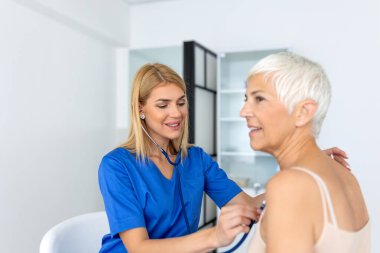 Bakıcı kadın doktor hastanede muayenede yaşlı hasta kalp atışlarını kontrol etmek için fonendoskop kullanıyor. Kadın hemşire ya da pratisyen hekim steteskop kullanıyor. Klinikte kadınların kalp atışlarını dinle..