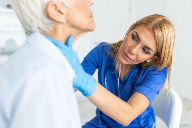 Klinikte kıdemli bir kadının boğazını inceliyor. Tiroid bezi testi olan kadınlar. Endokrinoloji, hormonlar ve tedavi. Boğaz iltihabı.
