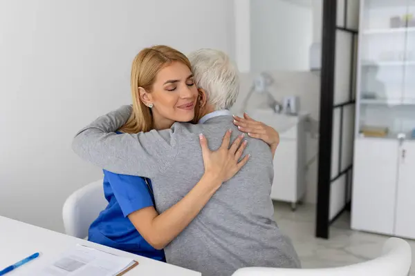 The elderly woman enjoys an embrace from her favorite healthcare doctor. Medical care, young female doctor hugging patient. Empathy concept. Elderly woman hugging caregiver