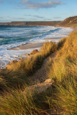Güneş batarken Cornwall 'daki Sennen Koyu' nun güzel manzarası karamsar gökyüzü ve uzun pozlu deniz hareketleriyle çimenli kum tepelerinden izleniyor.