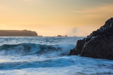 Corwnall İngiltere 'deki Kynance Koyu manzarası üzerinde göz kamaştırıcı bir gün doğumu canlı gökyüzü ve güzel turkuaz okyanusla