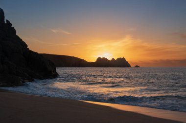 Cornwall İngiltere 'deki Porthcurno plajında büyüleyici renkler ve ruh haliyle güzel bir gün doğumu manzarası.