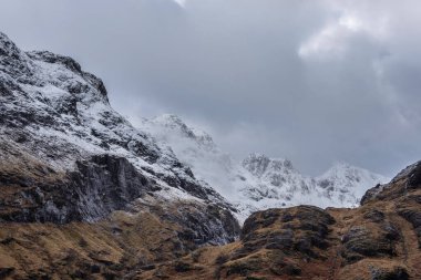 Glencoe İskoç dağlarında kar tepeli üç kız kardeşin dramatik gökyüzü eşliğinde destansı kış manzarası