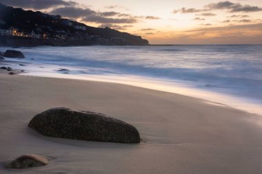 Güneş batarken Cornwall 'daki Sennen Koyu' nun güzel manzarası kasvetli gökyüzü ve uzun süre deniz hareketleriyle