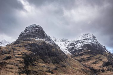 Glencoe İskoç dağlarında kar tepeli üç kız kardeşin dramatik gökyüzü eşliğinde destansı kış manzarası