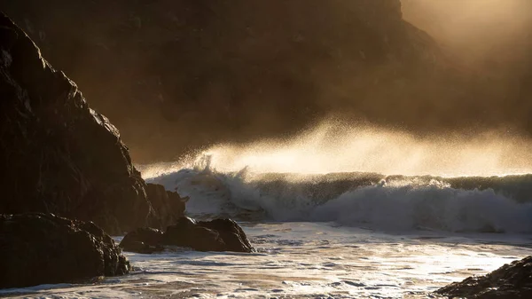 Kynance Coveコーンウォールの海岸と岩に輝く日の出の背景と風の水噴霧液滴にクラッシュする玉トルコ石の波の壮大な風景画像 — ストック写真