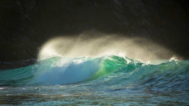 Yeşim turkuaz dalgaların kıyıya çarptığı destansı manzara görüntüsü ve Kynance Cove Cornwall 'daki kayalar, parlayan gündoğumu arka planı ve rüzgardaki su damlacıkları.