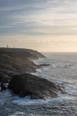 Günbatımında Cornwall uçurumunun muhteşem manzarası. Pendeen Deniz Feneri Burnu 'ndan arka planda kalay madenleri görülüyor.
