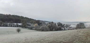 Şafak vakti, İngiliz kırsalında, ağaçların ve binaların karla kaplandığı sisli, güzel, rüzgarlı bir çiftlik manzarası.