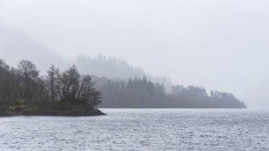 Beautiful calm peaceful Winter landscape over Thirlmere in Lake District with fog and layers of trees visible in the distance