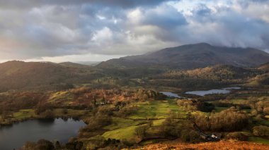 Beautiful Winter sunrise landscape view from Loughrigg Fell across Loughrigg Tarn with colorful dappled sunlight