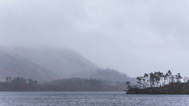 Beautiful calm peaceful Winter landscape over Thirlmere in Lake District with fog and layers of trees visible in the distance