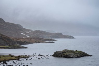 Beautiful dramatic Winter foggy landscape image of Wast Water in English Lake District with thick fog blocking view of mountains in distance