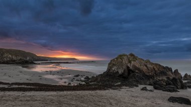 Cornwall 'daki Kennack Sands' in büyüleyici gündoğumu görüntüsü dramatik karamsar bulutlar ve canlı güneş patlaması