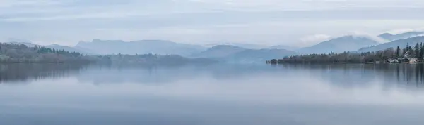 湖区温德尔米尔上空 湖面上停着小船和遥远的雾峰 令人叹为观止的春雾清澈的景象 免版税图库照片