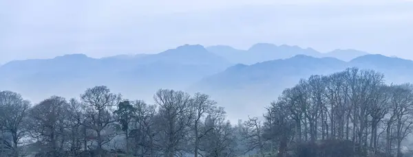 湖区温德尔米尔上空 湖面上停着小船和遥远的雾峰 令人叹为观止的春雾清澈的景象 图库图片