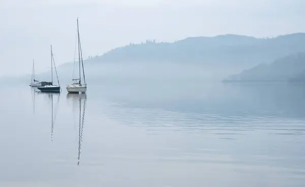 湖区温德尔米尔上空 湖面上停着小船和遥远的雾峰 令人叹为观止的春雾清澈的景象 图库图片
