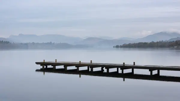 湖区温德尔米尔上空 湖面上停着小船和遥远的雾峰 令人叹为观止的春雾清澈的景象 免版税图库照片