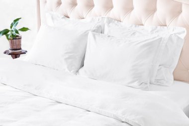 Yataklı yatak odası, beyaz yatak örtüsü ve komodinli. Beyaz yastıklar, yorgan ve yorgan kılıfı bej başlıklı yatakta. Temiz beyaz yastıklı yatak ve güzel yatak odasındaki çarşaflar..